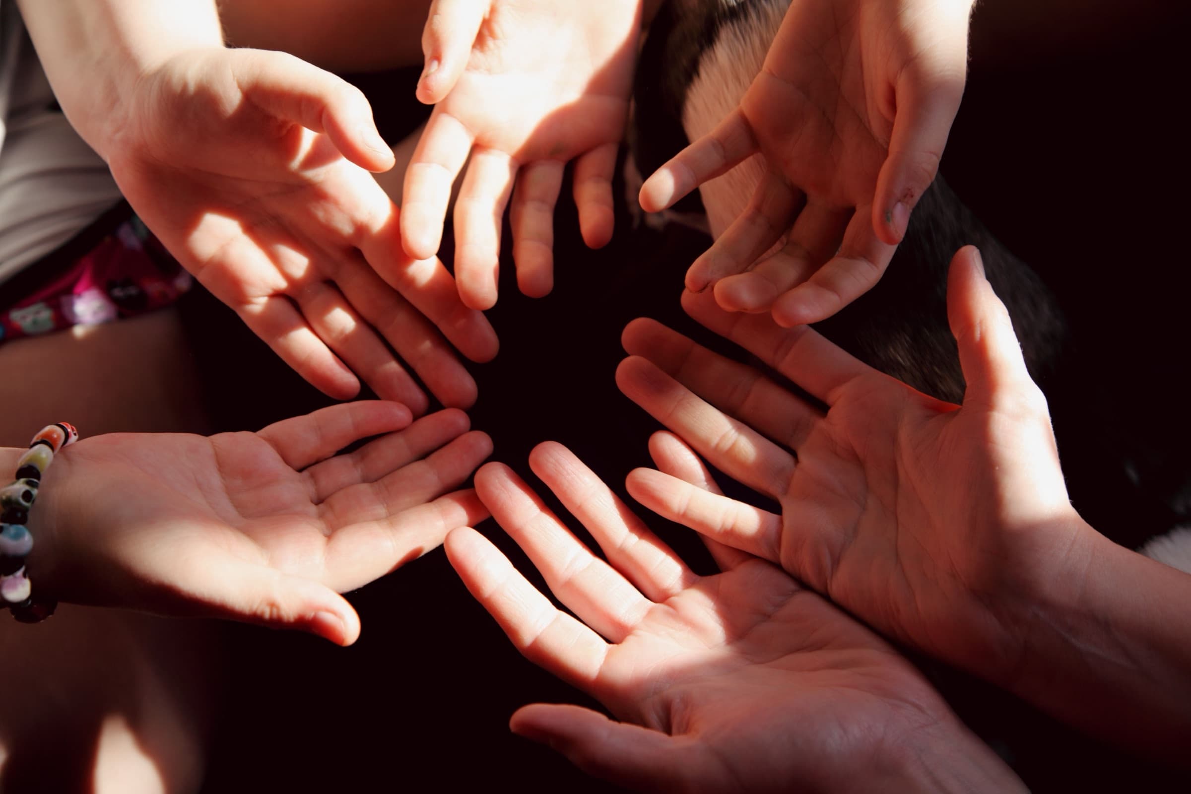 Open hands of several people forming a circle, joined to help